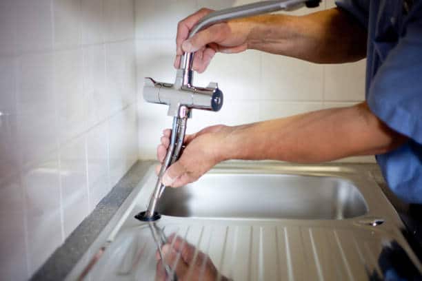 Gros plan sur les mains d'un plombier qui répare un robinet de cuisine