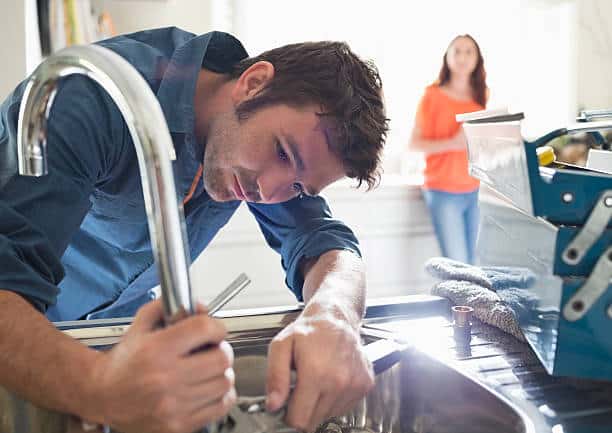 Plombier qui répare un évier de cuisine avec la cliente en arrière-plan